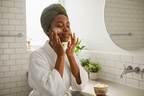 a african woman applying shea butter to her face in the bachroom